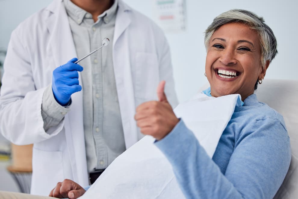 Middle aged woman sitting in a dental chair giving a thumbs up