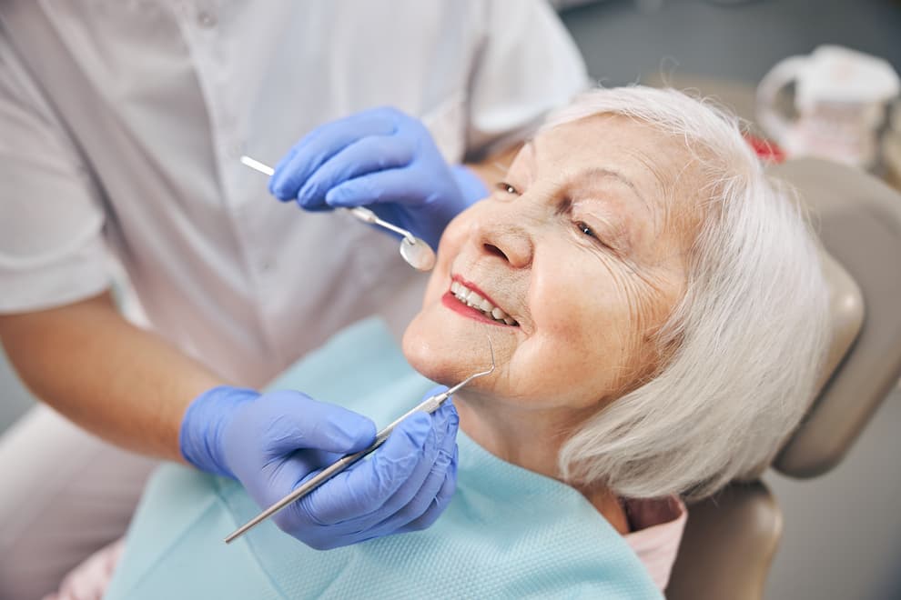 Older woman sitting in a dental chair with a dentist holding dental tools near her mouth